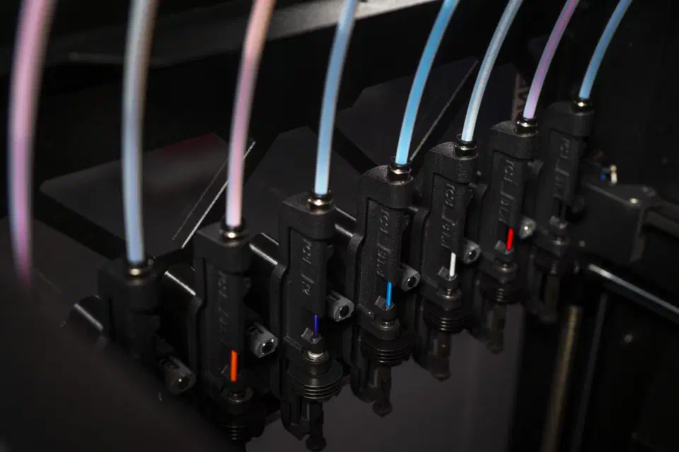 Eight black Bondtech INDX nozzle tools parked side by side inside a Prusa CORE One, each with a coloured filament tube feeding in from above