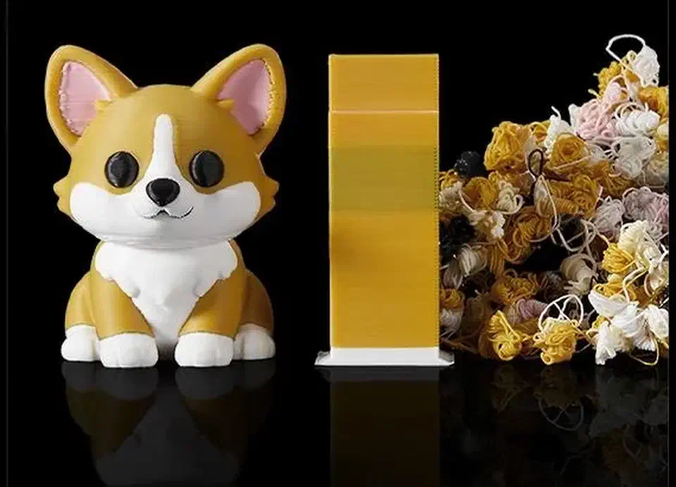 A printed two-colour corgi figure beside a yellow purge tower and a large pile of discarded purge blobs