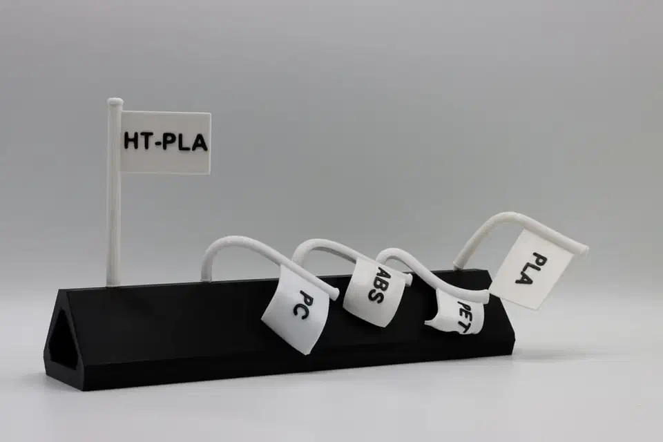 Oven heat test showing an HT-PLA flag standing upright while PC, ABS, PET, and PLA flags droop and curl over from the heat