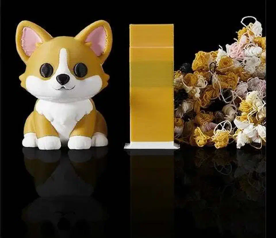 A small printed corgi model beside its yellow purge tower and a heap of discarded purge strings