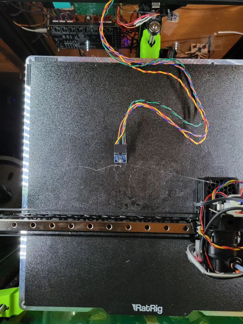 ADXL345 accelerometer breakout board resting on a textured black print bed, wired back to the toolhead for a Z resonance test