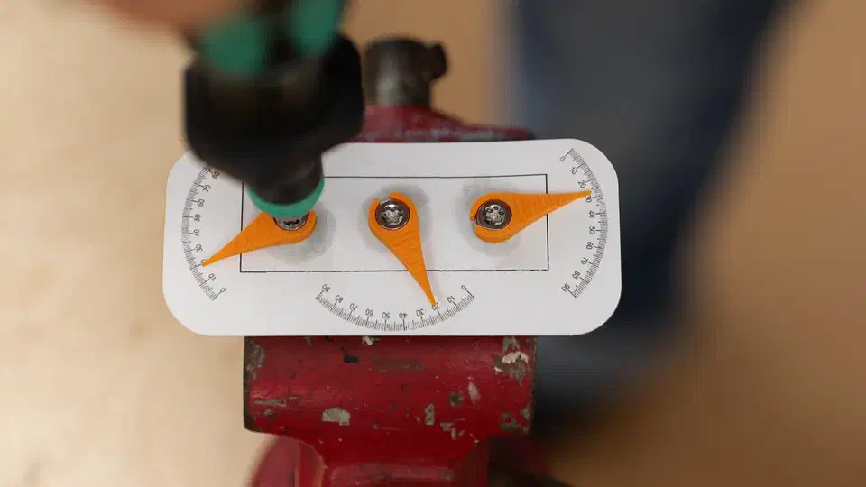 Three 3D-printed orange pointer needles on a protractor scale measuring bolt pretension loss in a torque test rig