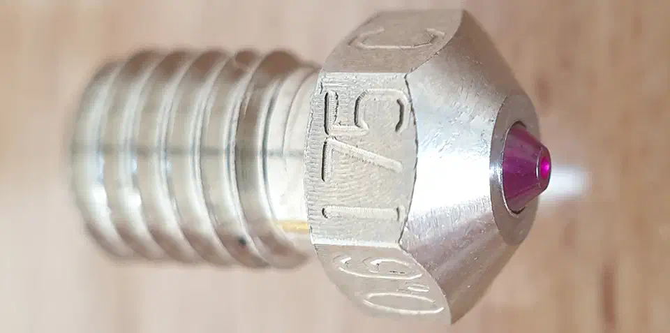 Side macro of a plated copper alloy ruby nozzle marked 0.6 and C, with the red ruby cone visible at the tip