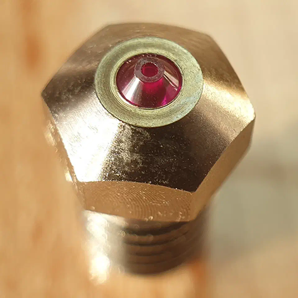 Macro end-on view of a brass nozzle with a small red ruby cone set flush in a steel washer at its centre