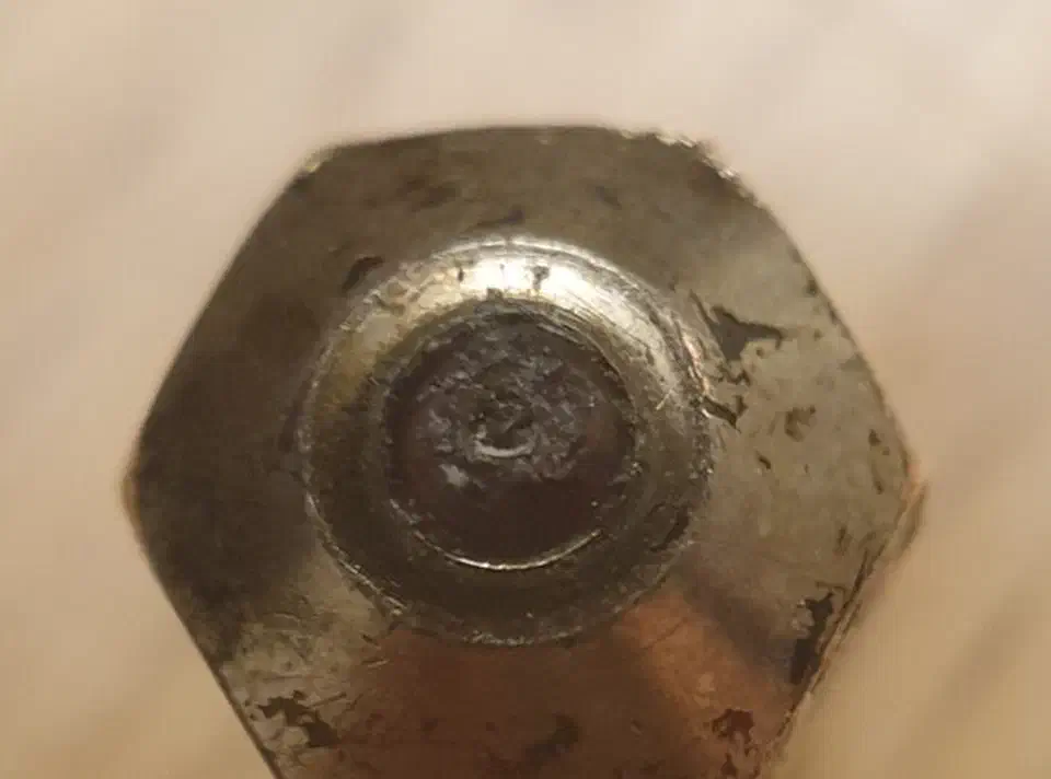 Macro view of a hexagonal nozzle face with a worn ruby tip showing irregular, pitted edges