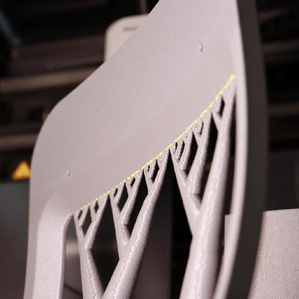 Close-up of a curved grey PPS-GF20 print with lattice tree supports and a yellow interface layer separating them from the part