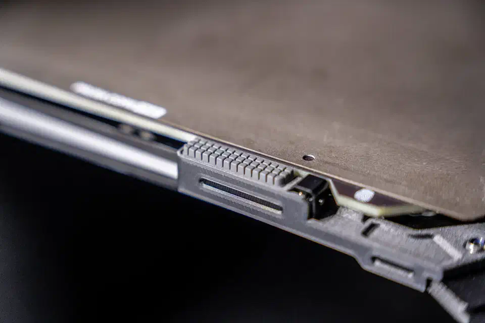 Close-up of a grey ridged nozzle wiper block mounted at the front edge of a Prusa print bed