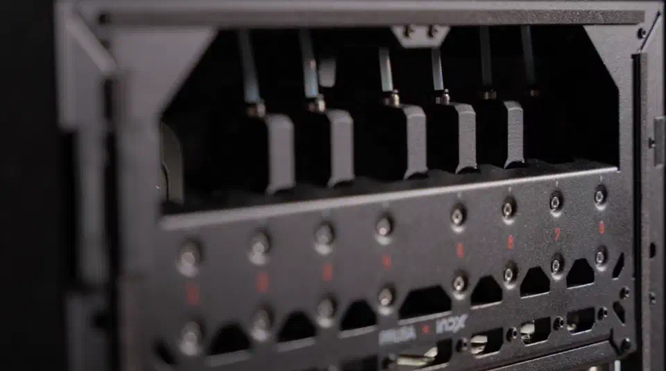 The INDX docking panel bolted across the front of the print chamber, a perforated black plate with eight numbered mounting positions holding the parked tools