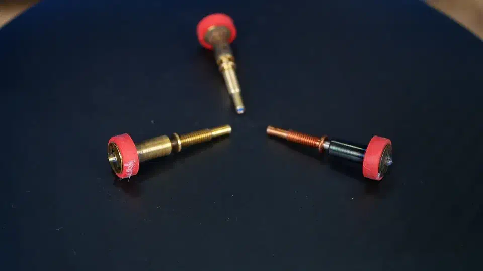 Three Revo nozzles laid on a dark surface, two with brass bodies and red silicone socks and one with a copper and dark coated body