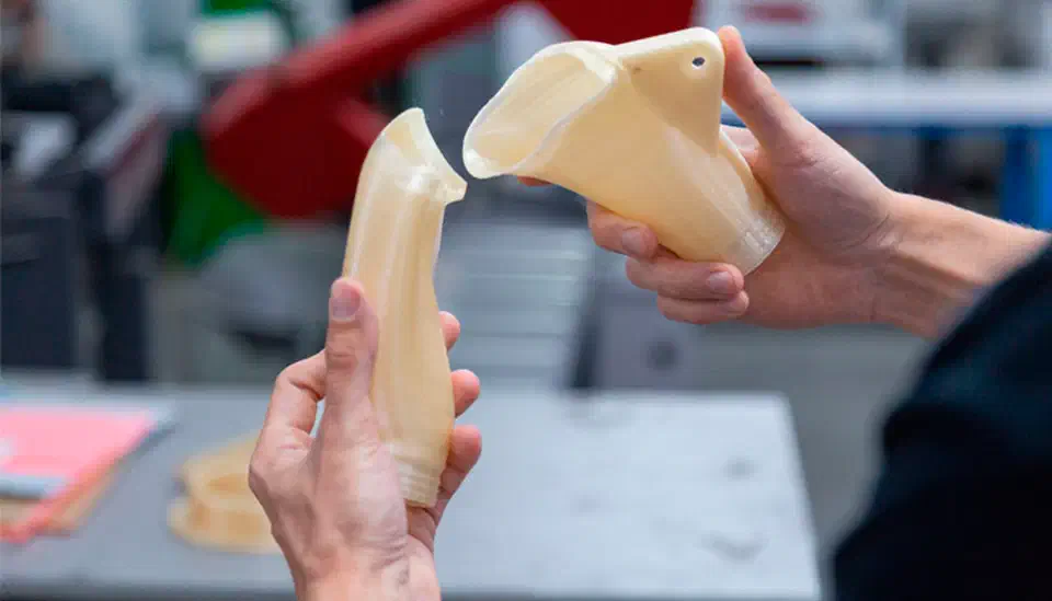 Two hands holding cream-colored 3D printed PPSU parts in a workshop