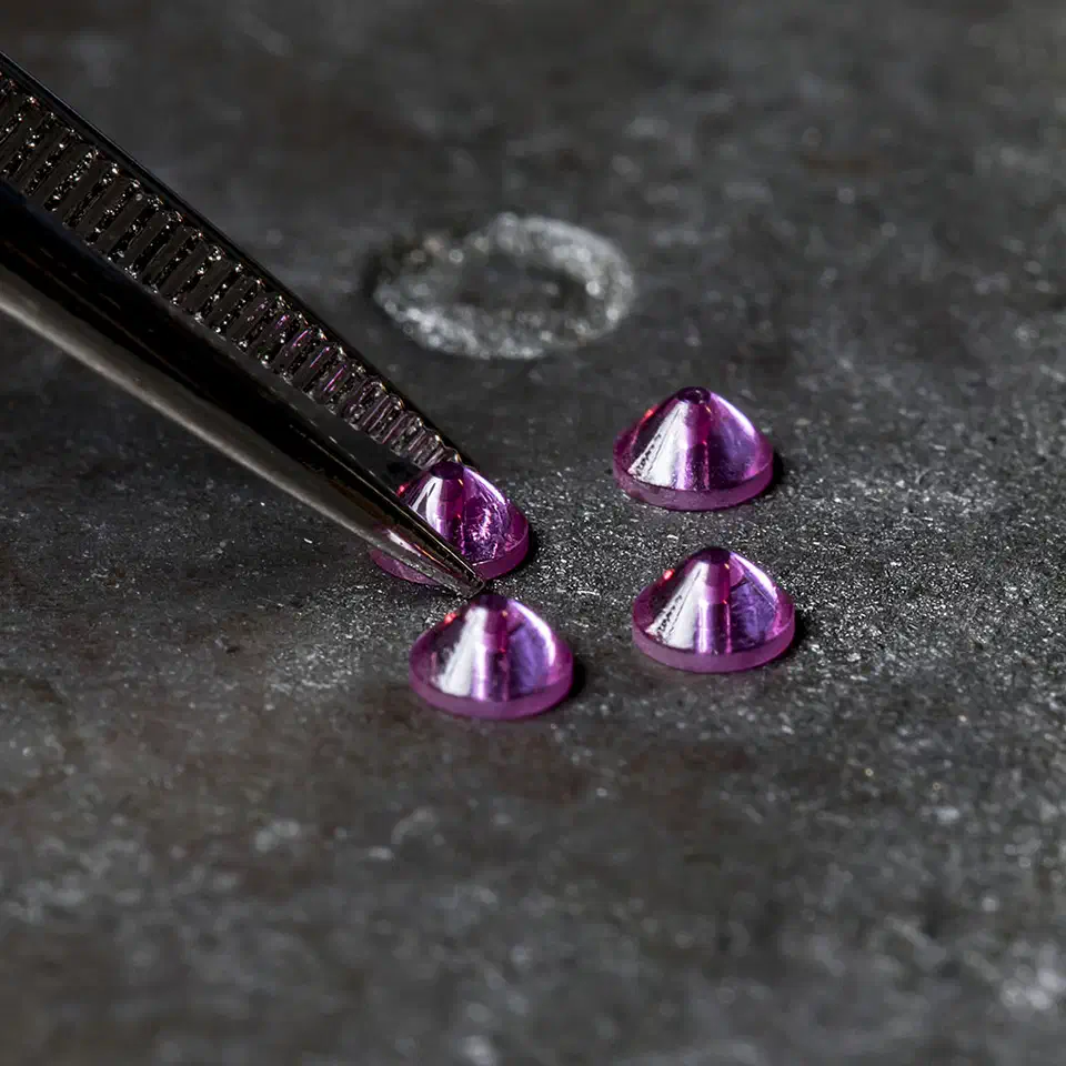 Four loose synthetic ruby nozzle tips, cone-shaped and deep pink, on a dark surface beside fine tweezers holding a fifth