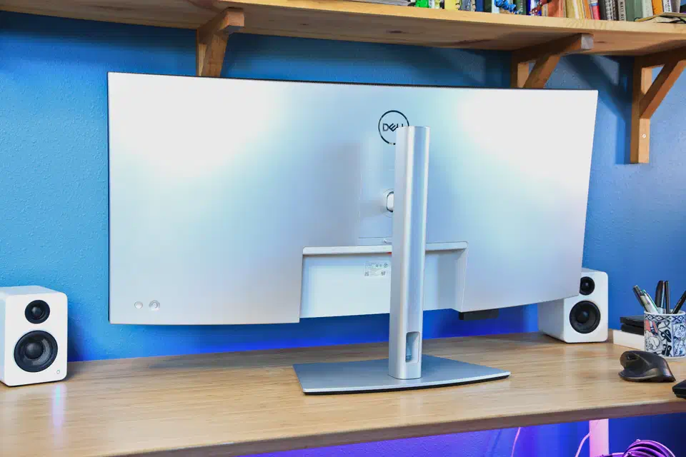 Rear of the Dell U4025QW on a desk, showing the white curved backplate, the central silver stand pillar, and the VESA mounting square