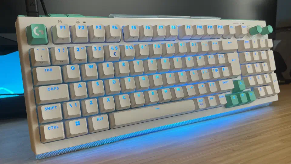 White G512 X on a wooden desk with blue backlighting glowing through the keycap legends and under the front lip