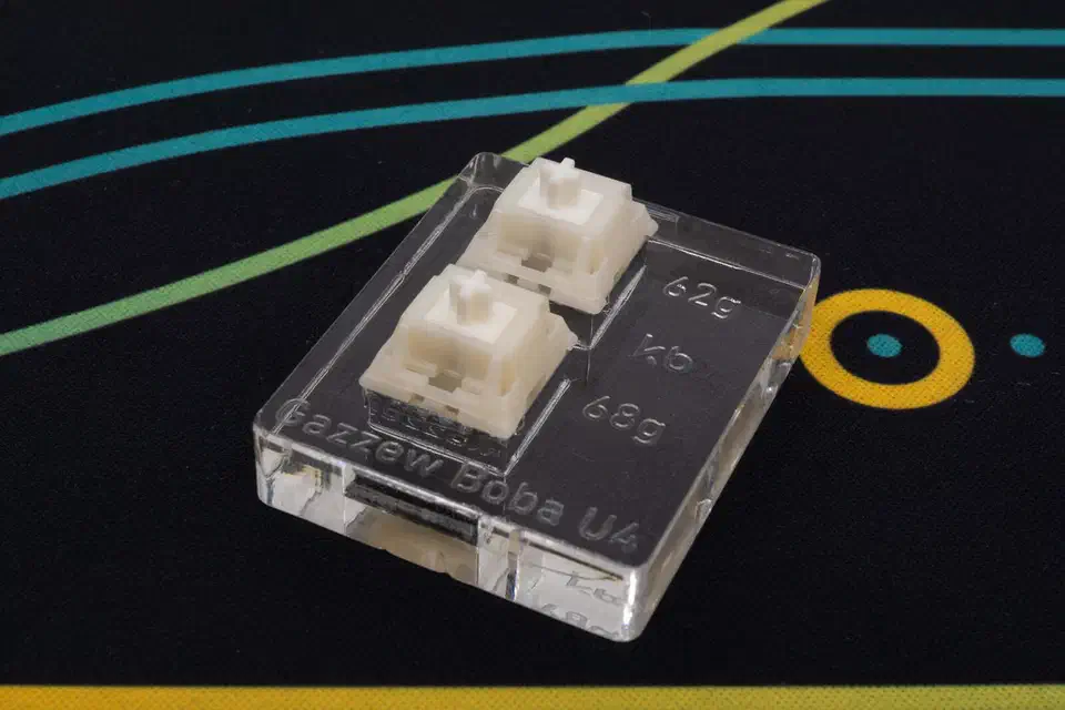 Clear Gazzew Boba U4 switch tester holding two switches, with 62g, 65g, and 68g weight slots labeled
