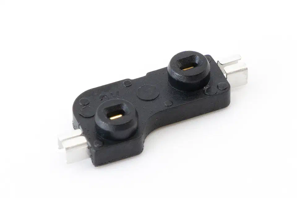Close-up of a single black Kailh socket showing two pin-entry holes with gold contact leaves inside and silver solder tabs