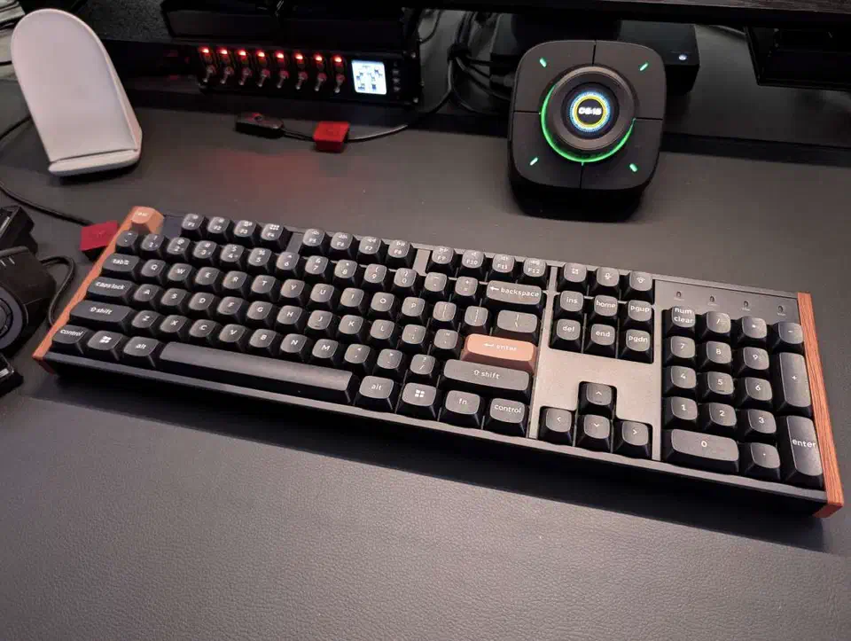 Keychron K10 HE full-size keyboard on a desk showing the wood side panels, grey keycaps and orange accent keys