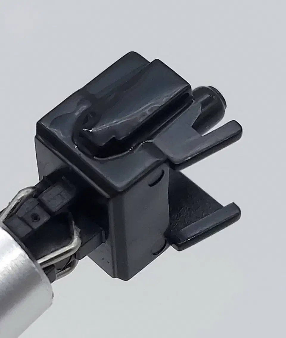 Close-up of a black Gateron Oil King stem held in tweezers with a glossy factory lubrication coat on its rails