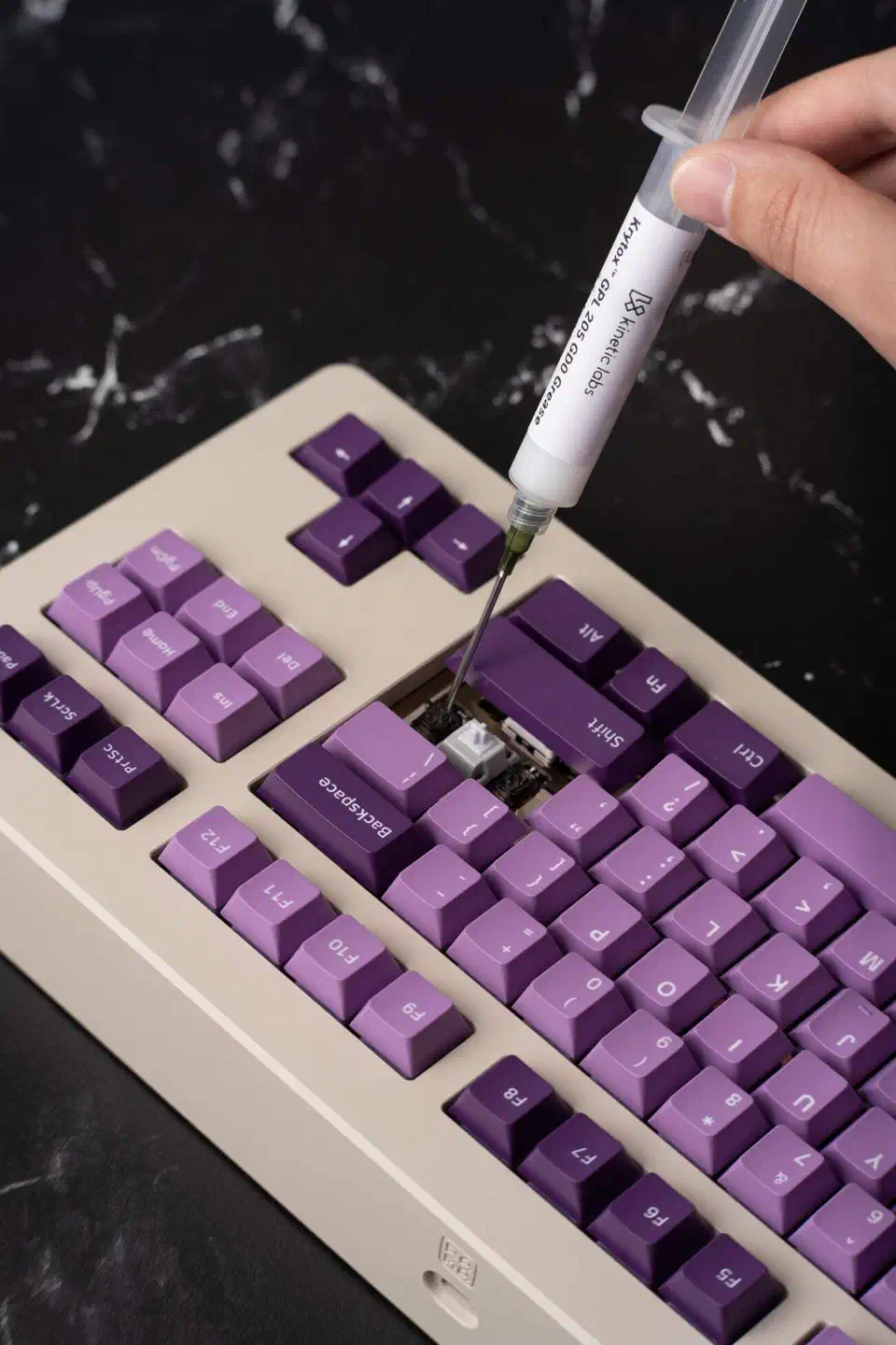 Krytox GPL 205 GD0 grease syringe with a fine needle tip applying lube to a switch on a cream keyboard with purple keycaps