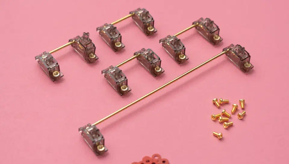 Six Durock V2 screw-in stabilizers with smoky translucent housings and gold wires beside a pile of gold screws