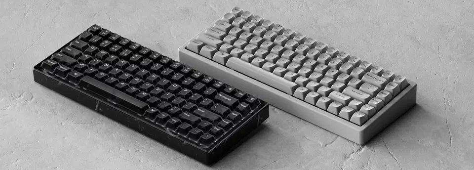 Keychron K2 HE Special Edition keyboards in black Resin and grey Concrete lying side by side on a stone surface