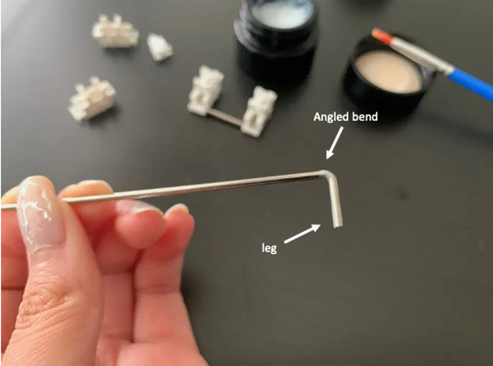 Hand holding a 6.25u stabilizer wire with white lube coated on the leg and the angled bend