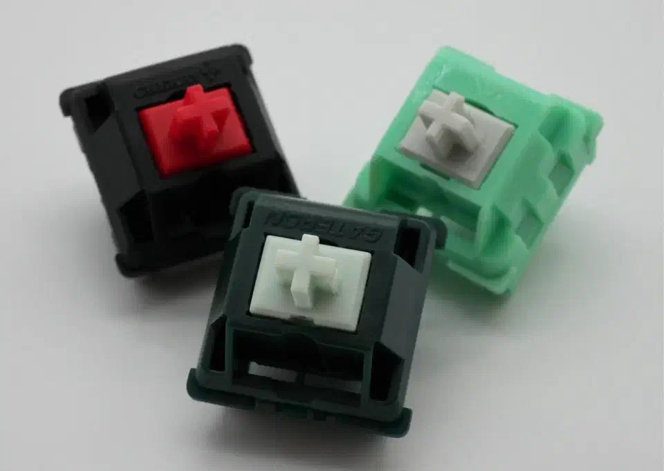 Keyboard switches that use basic single-stage springs, the Cherry MX Red, KTT Mint and Gecko Silent Linear, with their evenly wound coils visible