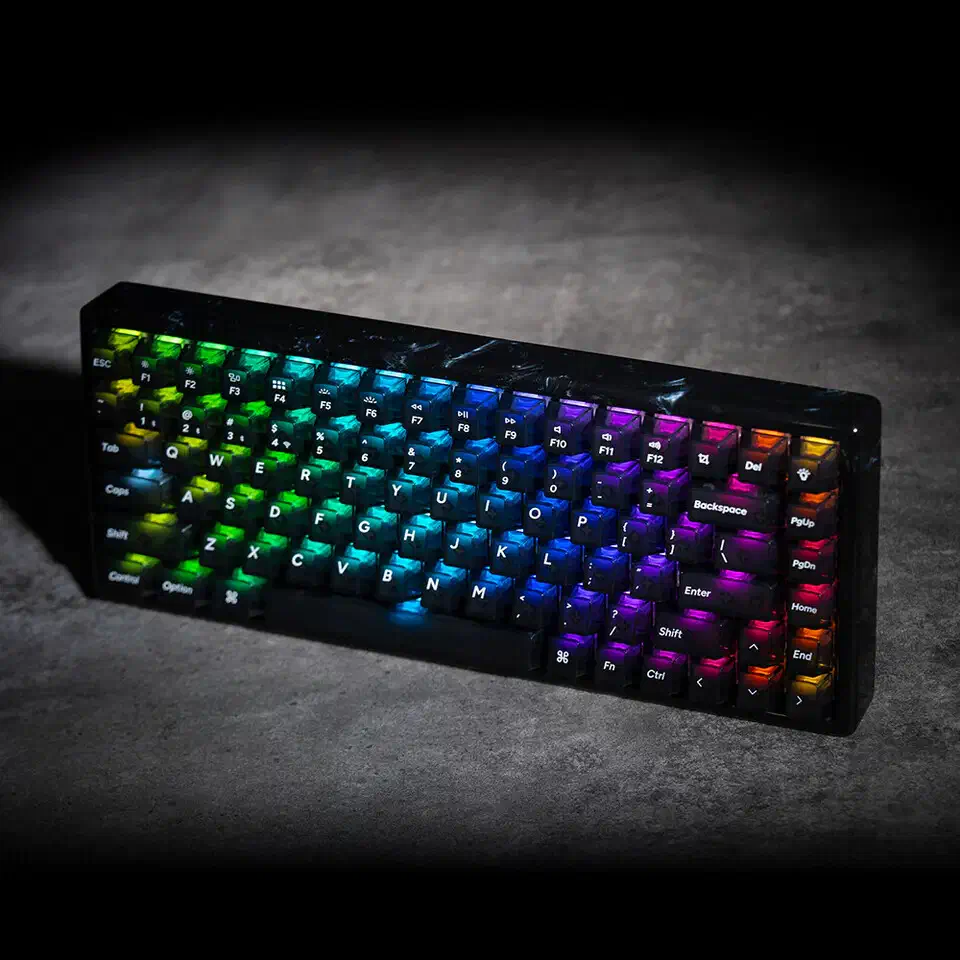 Keychron K2 HE Resin Edition on a dark stone surface with rainbow per-key RGB lighting glowing through its smoky transparent PC keycaps