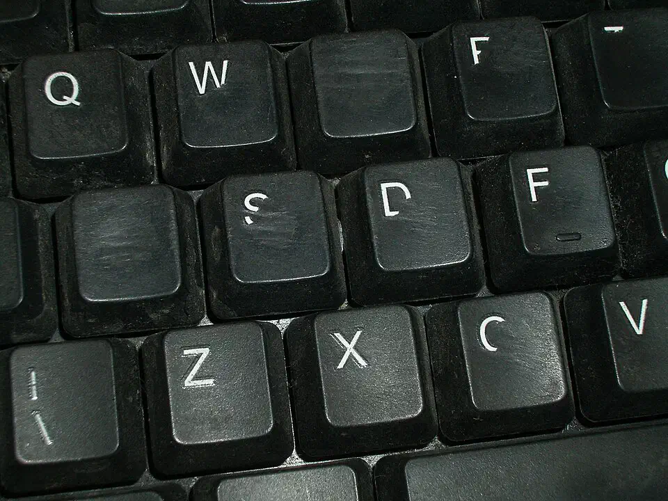 Worn black keycaps on a membrane keyboard with glossy rubbed patches on the Q, S and D keys and half-erased printed legends