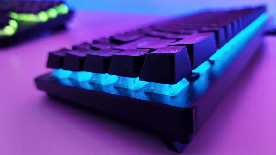 Low-angle close-up of the Huntsman V3 HE showing translucent switch housings lit cyan under black keycaps