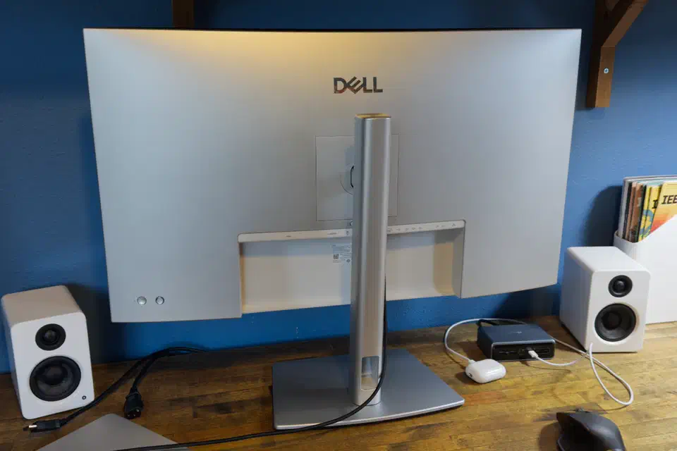 Rear three-quarter view of the Dell U3225QE showing the recessed port shroud and cable pass-through where the upstream cables land