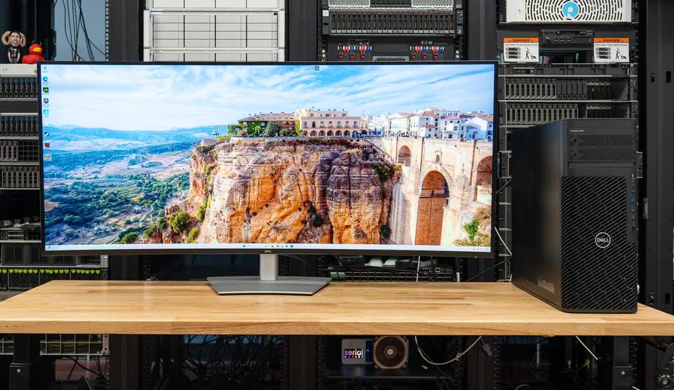 Dell UltraSharp U5226KW curved 52-inch ultrawide monitor on a wooden bench in front of server racks, with a Dell Precision tower beside it