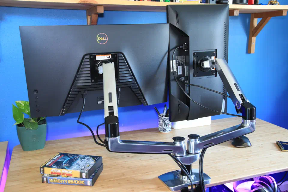 Two black monitors mounted on a polished silver Ergotron LX Pro dual gas-spring arm clamped to a wooden desk