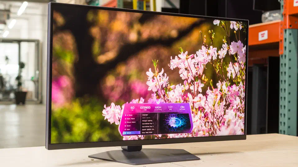 LG 27GM950B on its stand on a test bench, screen showing pink blossom against dark branches with the on-screen menu open