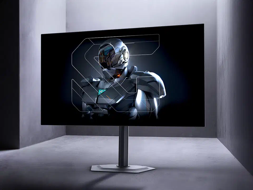 Gigabyte MO27Q28GR OLED gaming monitor on a fully adjustable stand in a grey studio, displaying an armoured figure on a dark background
