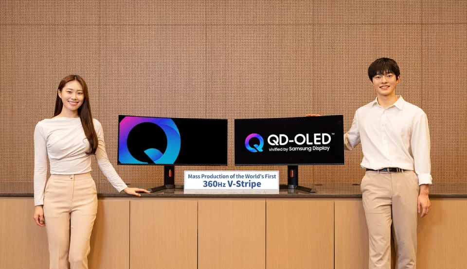 Two Samsung Display presenters standing beside a pair of curved 34-inch ultrawide QD-OLED panels, with a sign reading Mass Production of the World&rsquo;s First 360Hz V-Stripe between them