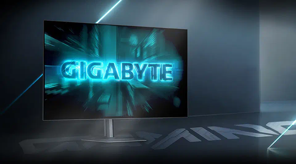 Gigabyte GO27Q24G on a white pillar stand in a dark room, glossy screen showing a bright cyan Gigabyte logo