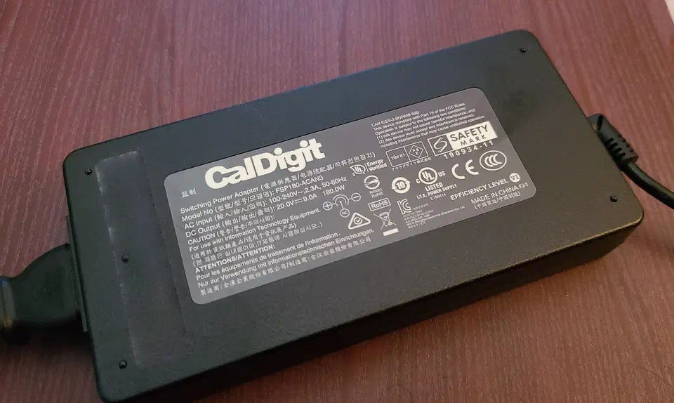 Large black external power brick for a docking station with a thick captive cable coiled beside it