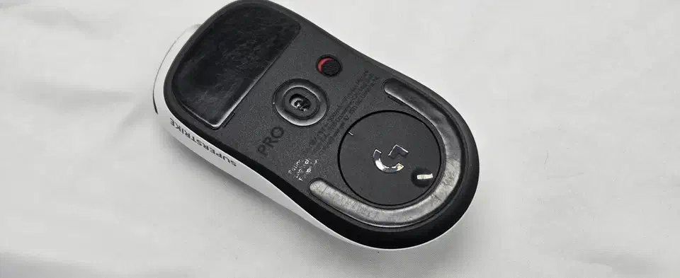 Underside of the white Logitech G Pro X2 Superstrike showing its two black stock skates, a large rectangular pad at the front and a U-shaped pad wrapping the rear sensor ring