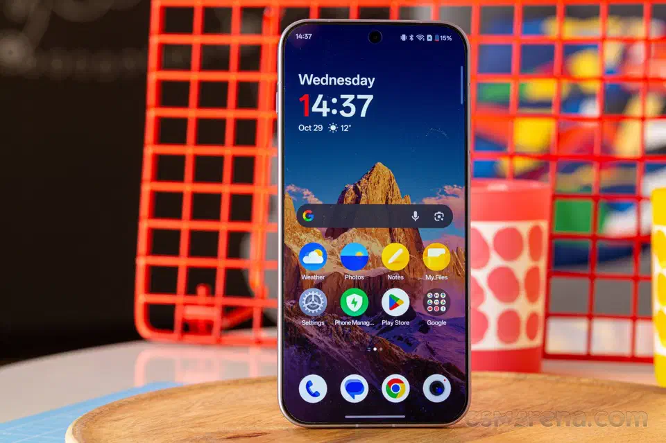 OnePlus 15 standing on a wooden table with its home screen lit and the battery indicator reading 15 percent