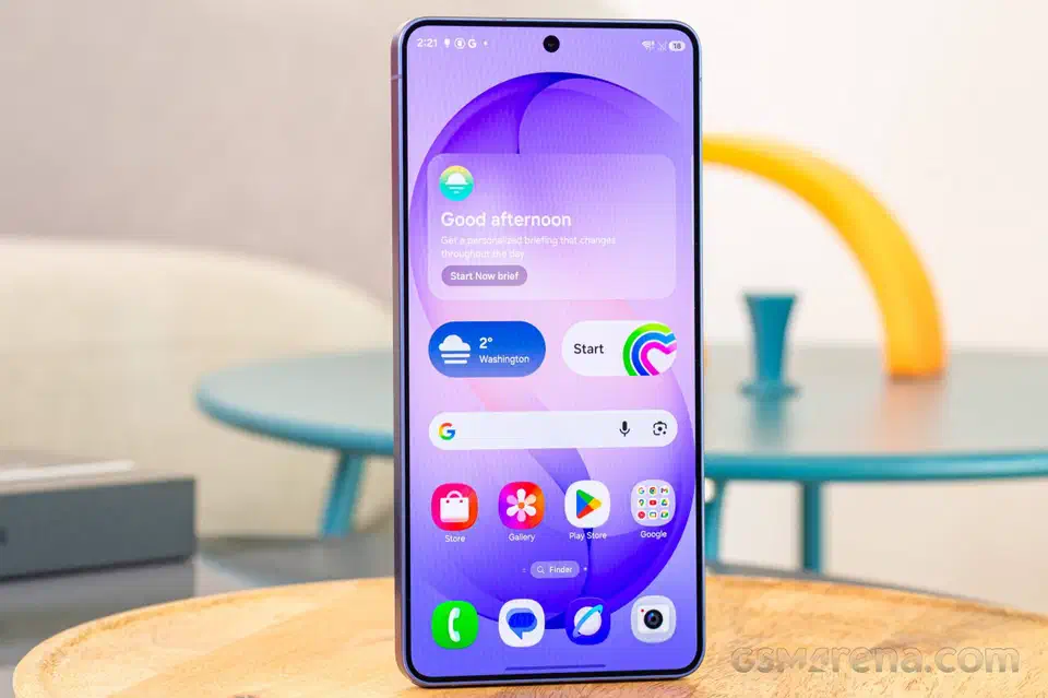 Galaxy S26 Ultra standing upright on a wooden table with its home screen lit, showing the 6.9-inch panel and slim violet frame
