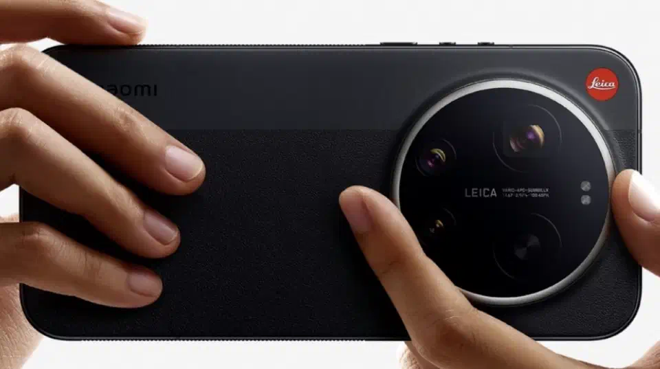 Two hands hold the black leather-backed Leica edition horizontally, one finger on the rotating ring, the other supporting the body