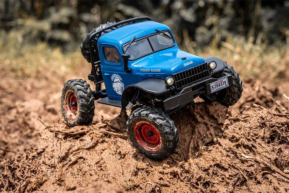 Blue FMS FCX24 Power Wagon 1/24 crawler climbing over a mound of mud outdoors