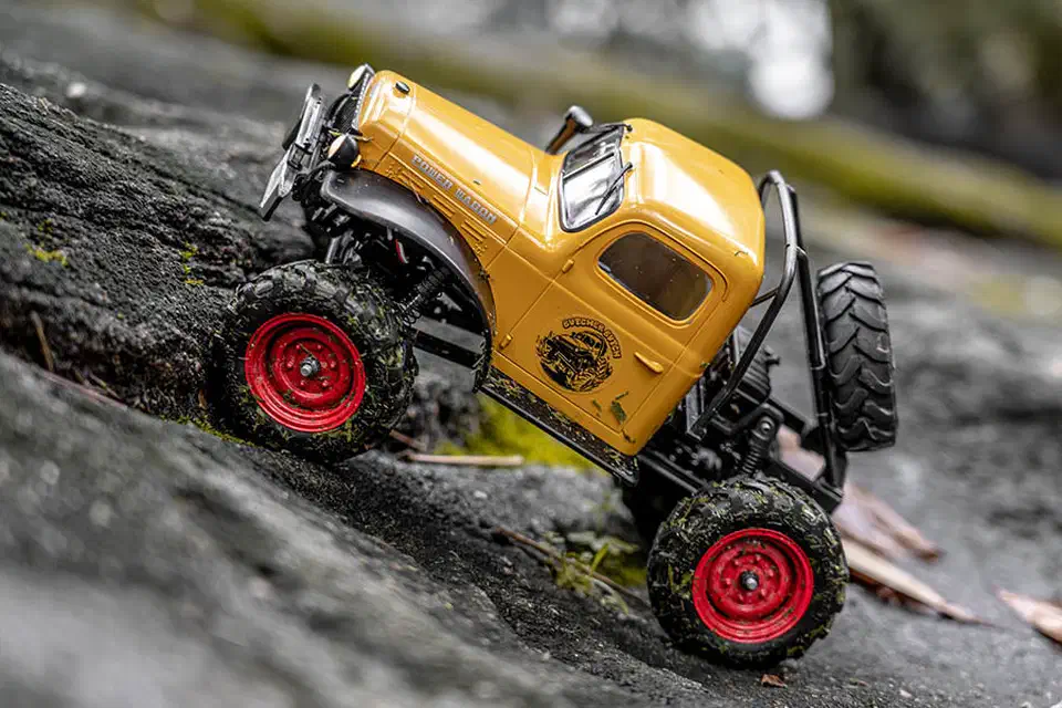 Yellow FMS FCX24 Power Wagon crawling up a mossy rock with its portal axles lifting the differentials clear
