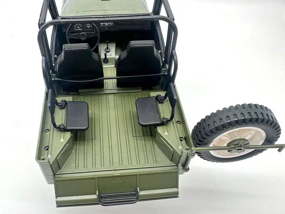 Overhead view into the WPL C84 cabin showing the black roll cage, folding front seats, two rear jump seats, the ribbed cargo floor and the open rear gate with a swing-out spare wheel